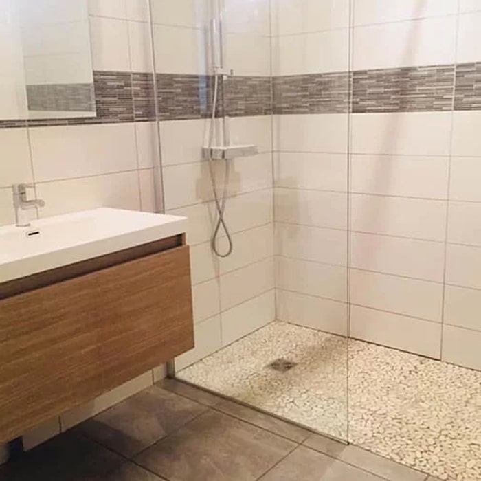 Douche à l'Italienne avec Sol en Galets et Meuble en Bois Douche à l'italienne moderne avec sol en galets, meuble sous-vasque suspendu en bois et carrelage mural beige.