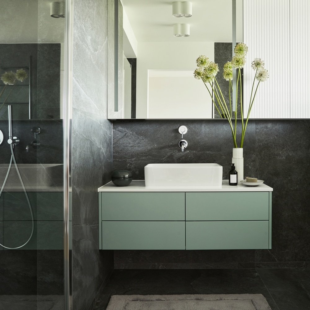 Meuble vasque vert sauge et salle de bain moderne chic Meuble vasque vert sauge suspendu dans une salle de bain moderne avec carrelage noir et vasque à poser blanche.