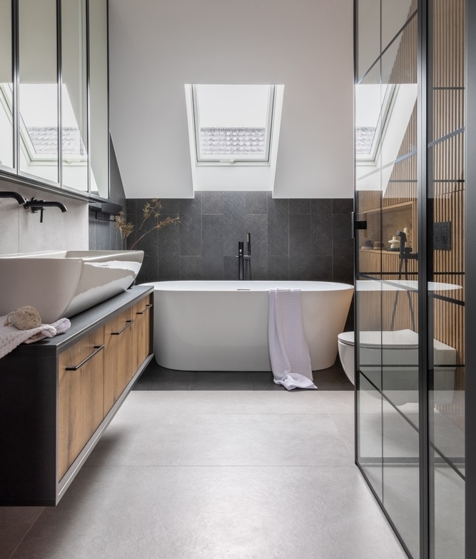 Design Salle de Bain Moderne : Baignoire îlot et Bois Salle de bain moderne avec baignoire îlot, vanité en bois, carrelage gris foncé et fenêtre de toit lumineuse.